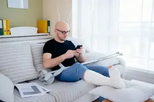 Injured man with crutches sitting on the couch on his phone.