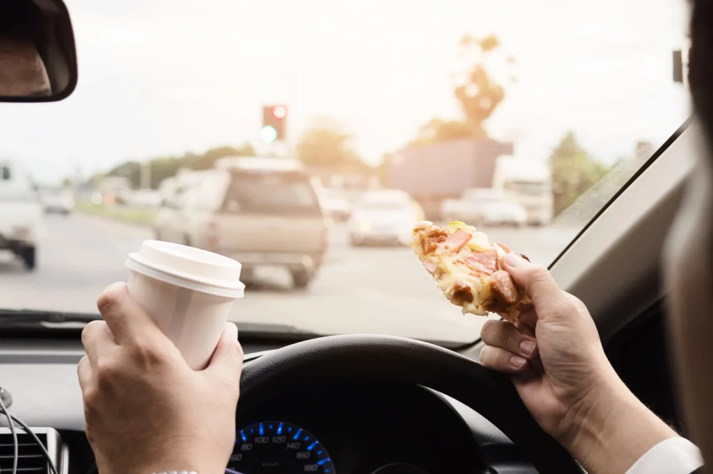 A person driving holding a paper cup and food.