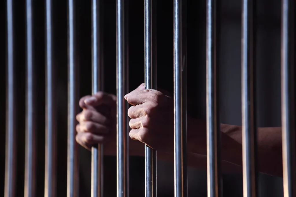 Person inside a prison cell, holding on to the bars.