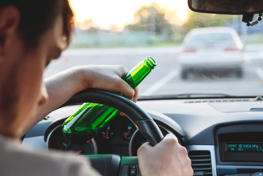 Man driving while drinking, holding a green bottle.