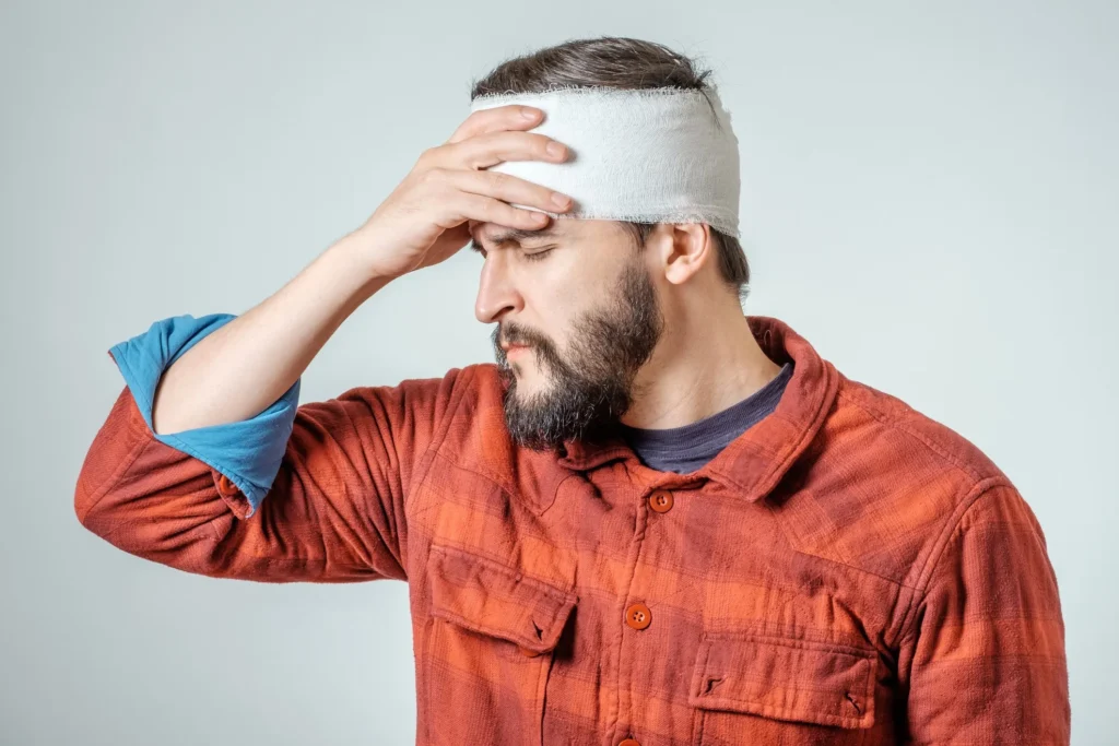 Person with a head bandage, holding his head.
