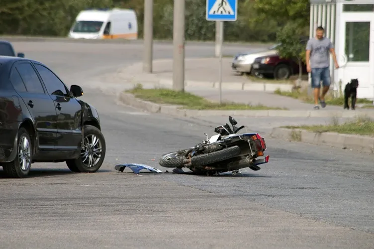 A crashed motorcycle on the road next to a car.