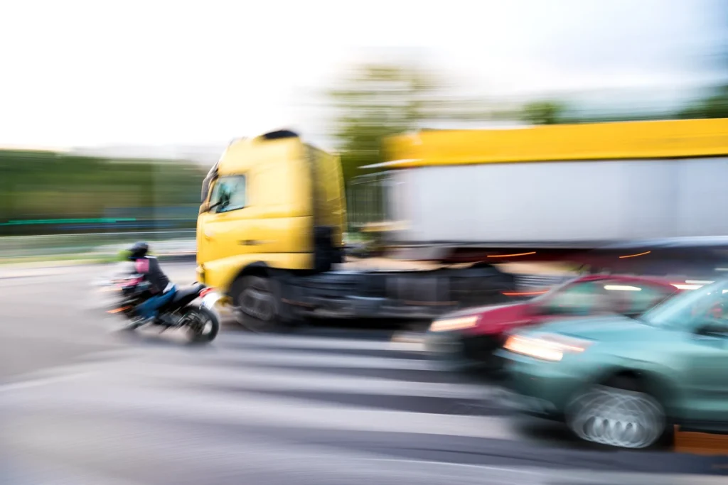 High-speed motorcyclist passing semi-truck on highway.